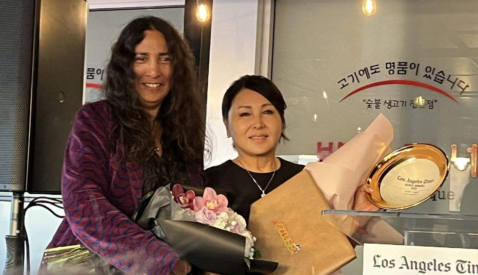지난 12일 LA 한인타운에 있는 식당 ‘박대감네’에서 사장 제니 김(오른쪽)씨가 LA타임스 관계자에게 상패와 꽃을 전해받고 웃고 있다. /박대감네 제공.